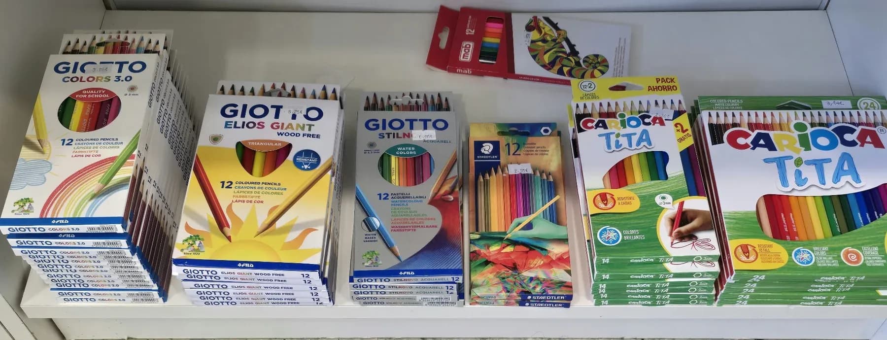 Caixas de lápis de cor de várias marcas alinhadas numa prateleira baixa